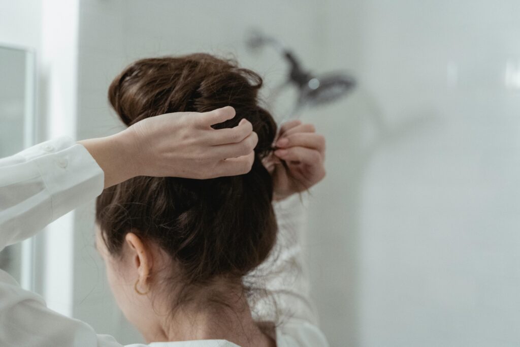 A woman styles her hair into an elegant bun in a bathroom setting, focusing on hair care.